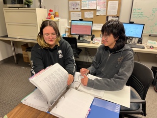 Two students reading a manuscript in a binder