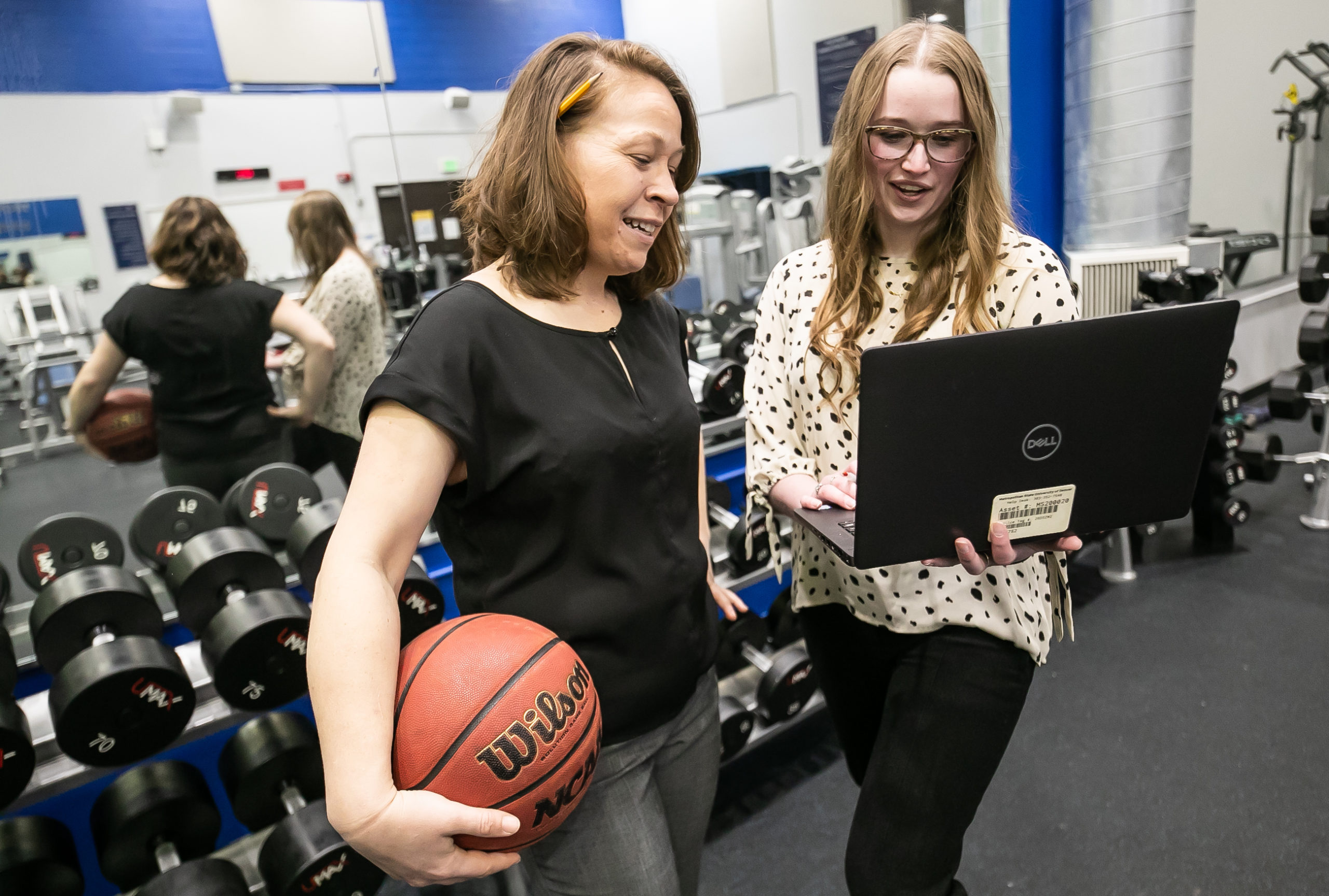 People standing in a gym, one is holding a basketball and the other a laptop