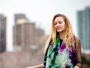 A woman meditating outside with Denver cityscape in background.