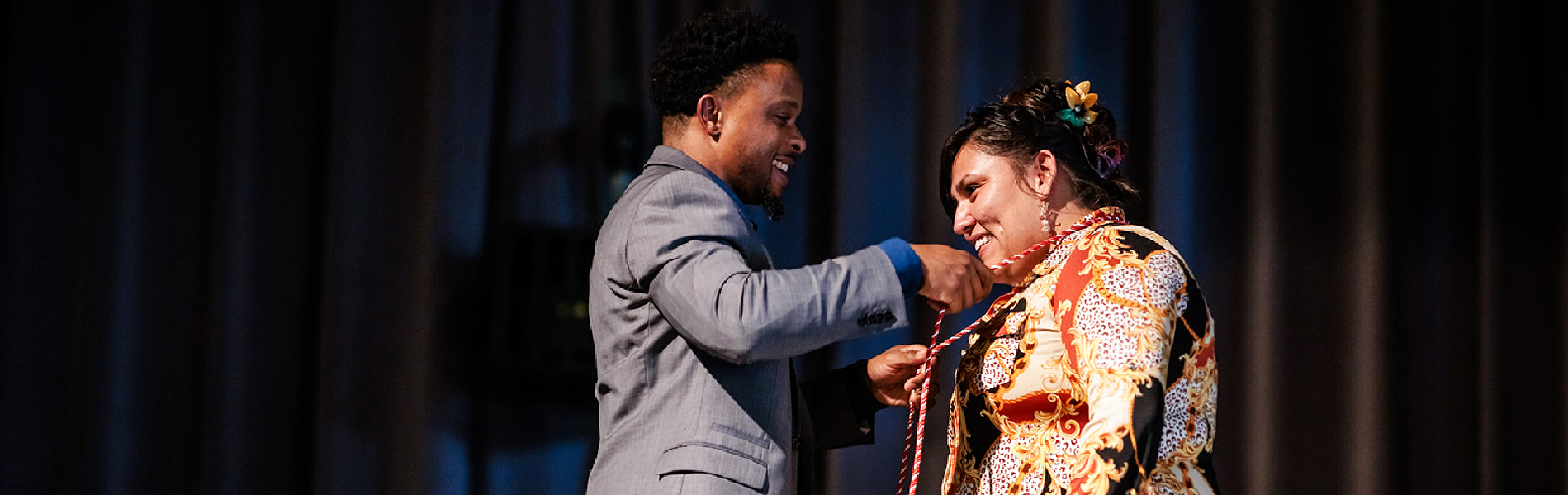 man placing honor cord on smiling graduate