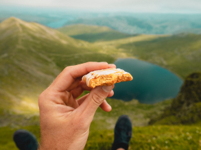 close up of someone holding up a snack with their feet mountains and lakes in the background