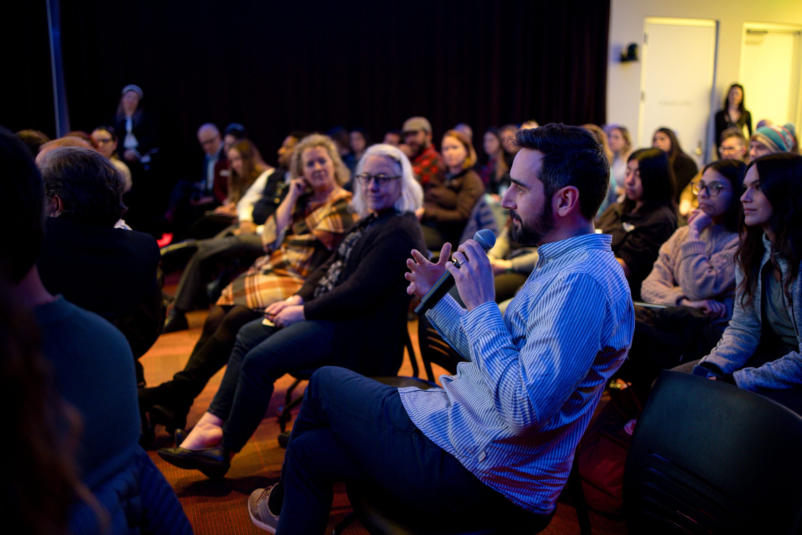 A person in an audience speaking into a microphone, asking a question of the people on stage.