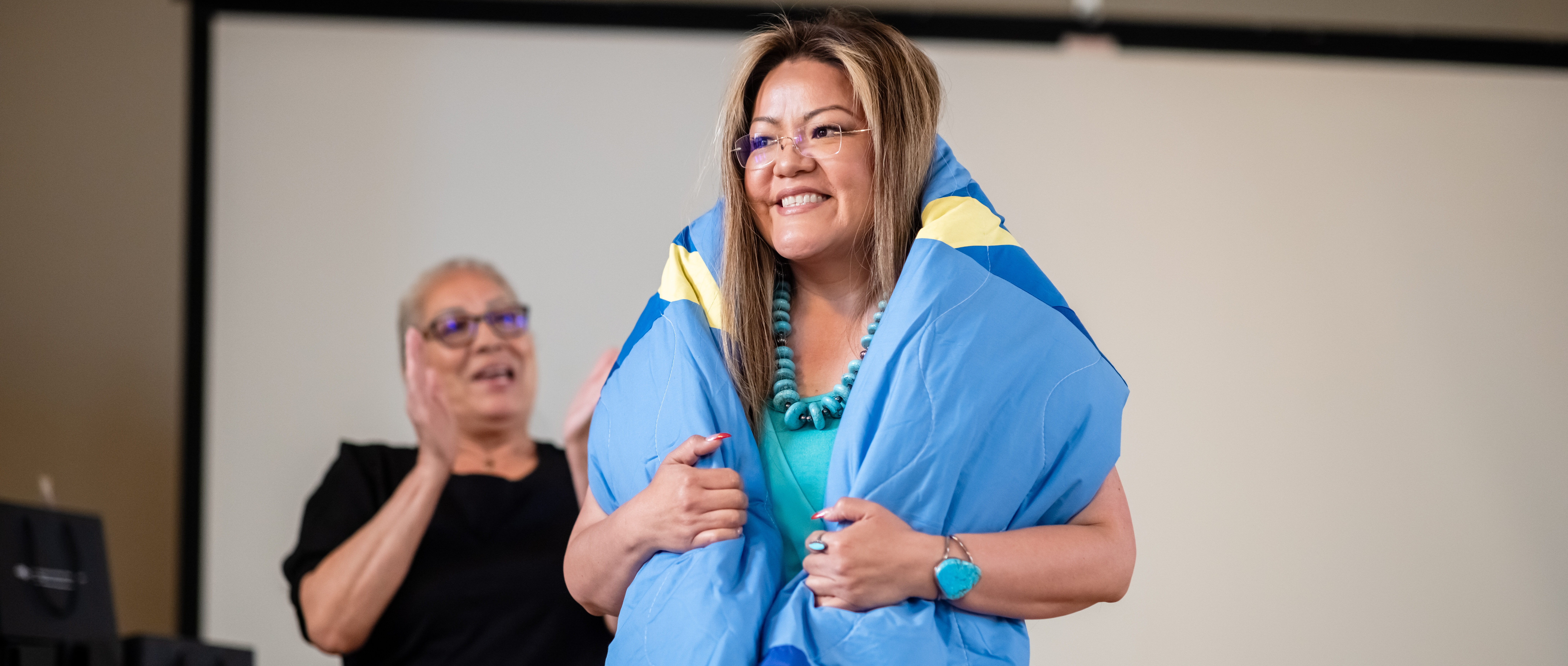 A graduate smiles while at their blanket wrapping ceremony.