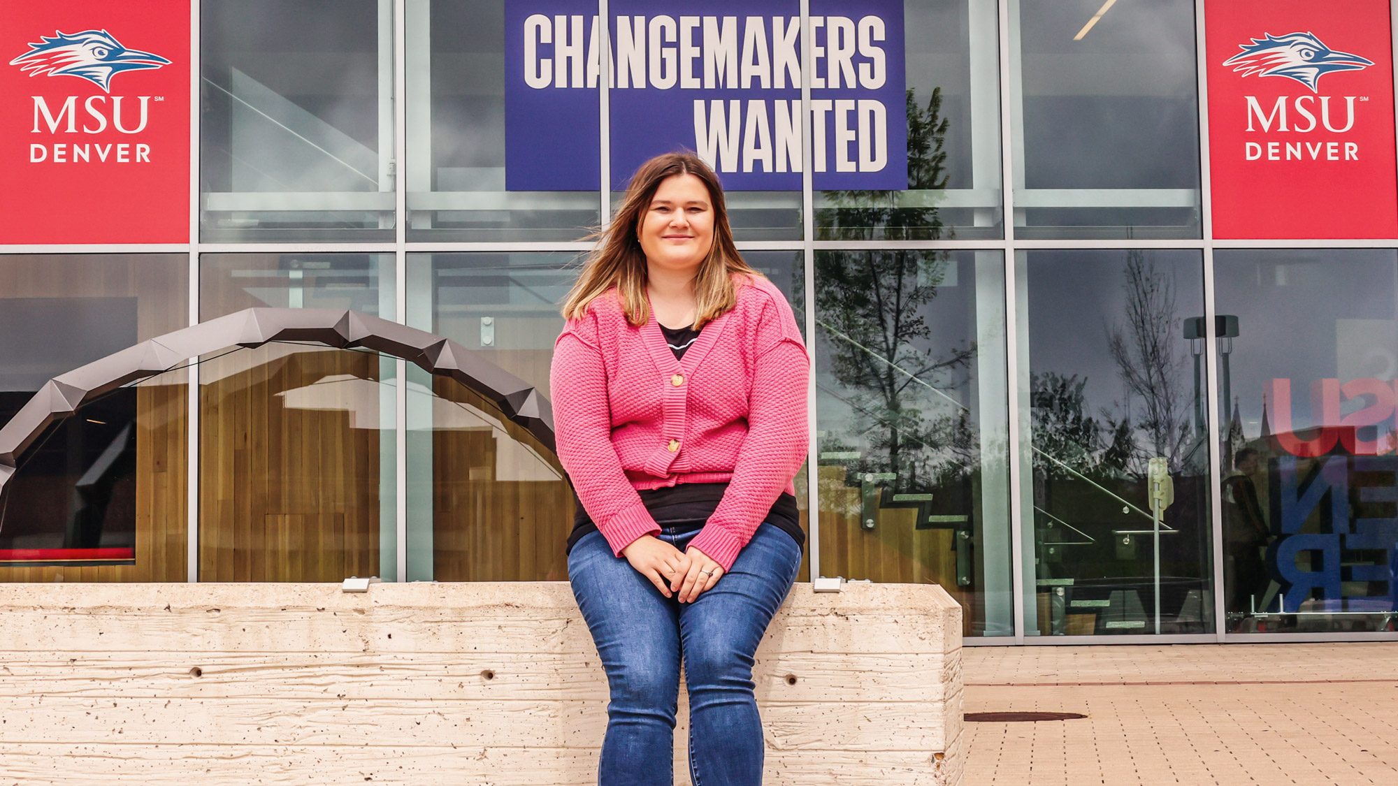 MSU Denver social work graduate student Christy Walker sits in front of the Changemakers Wanted sign on JSSB