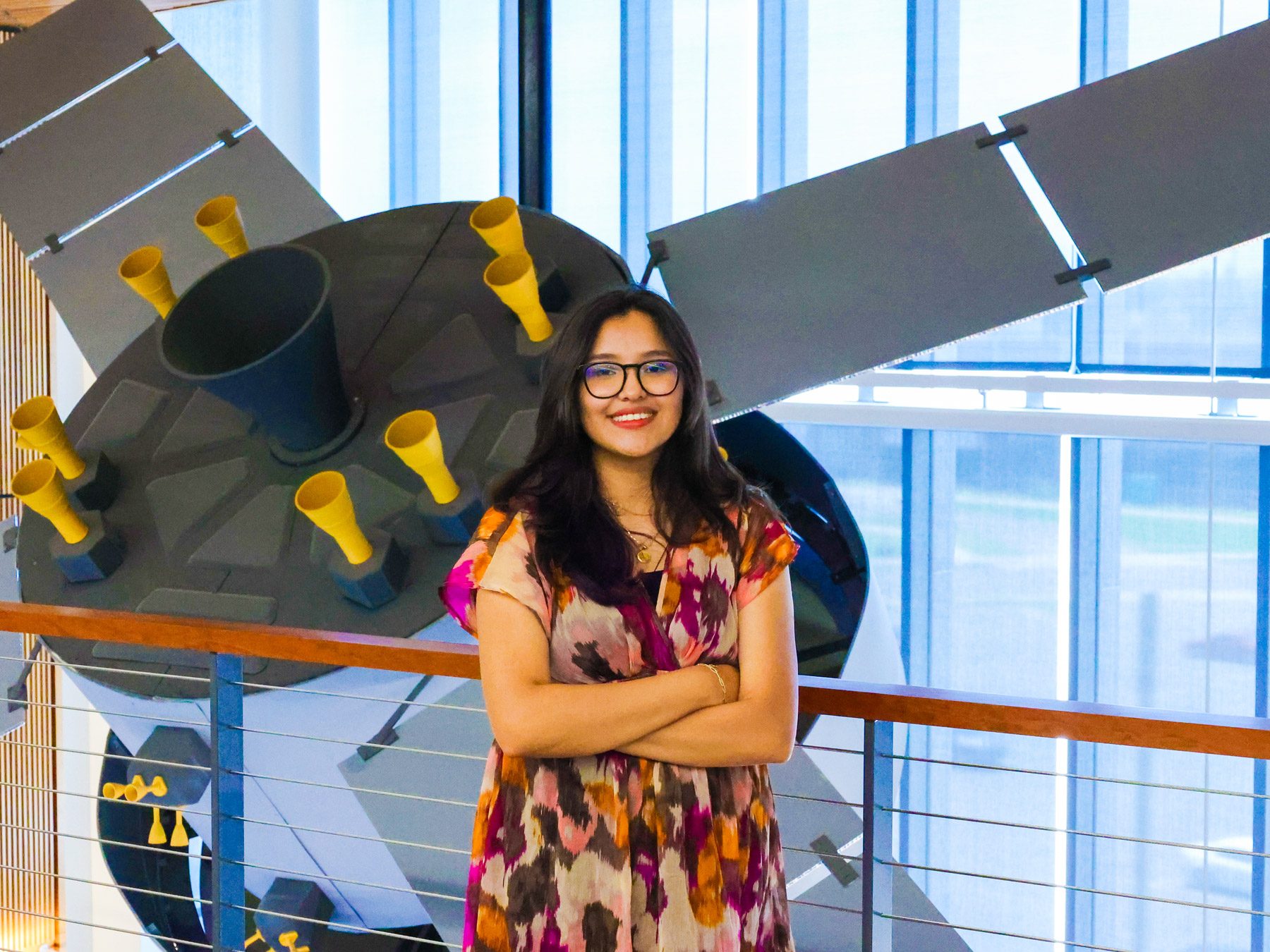 Aerospace engineering technology major Evelyn Montes Gonzalez standing in front of the satellite in the AES building