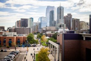 Aerial photo of students walking along Auraria Campus thoroughfare with Denver Downtown in background.