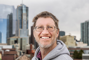 Dr. John Carter smiling with the Denver skyline behind him