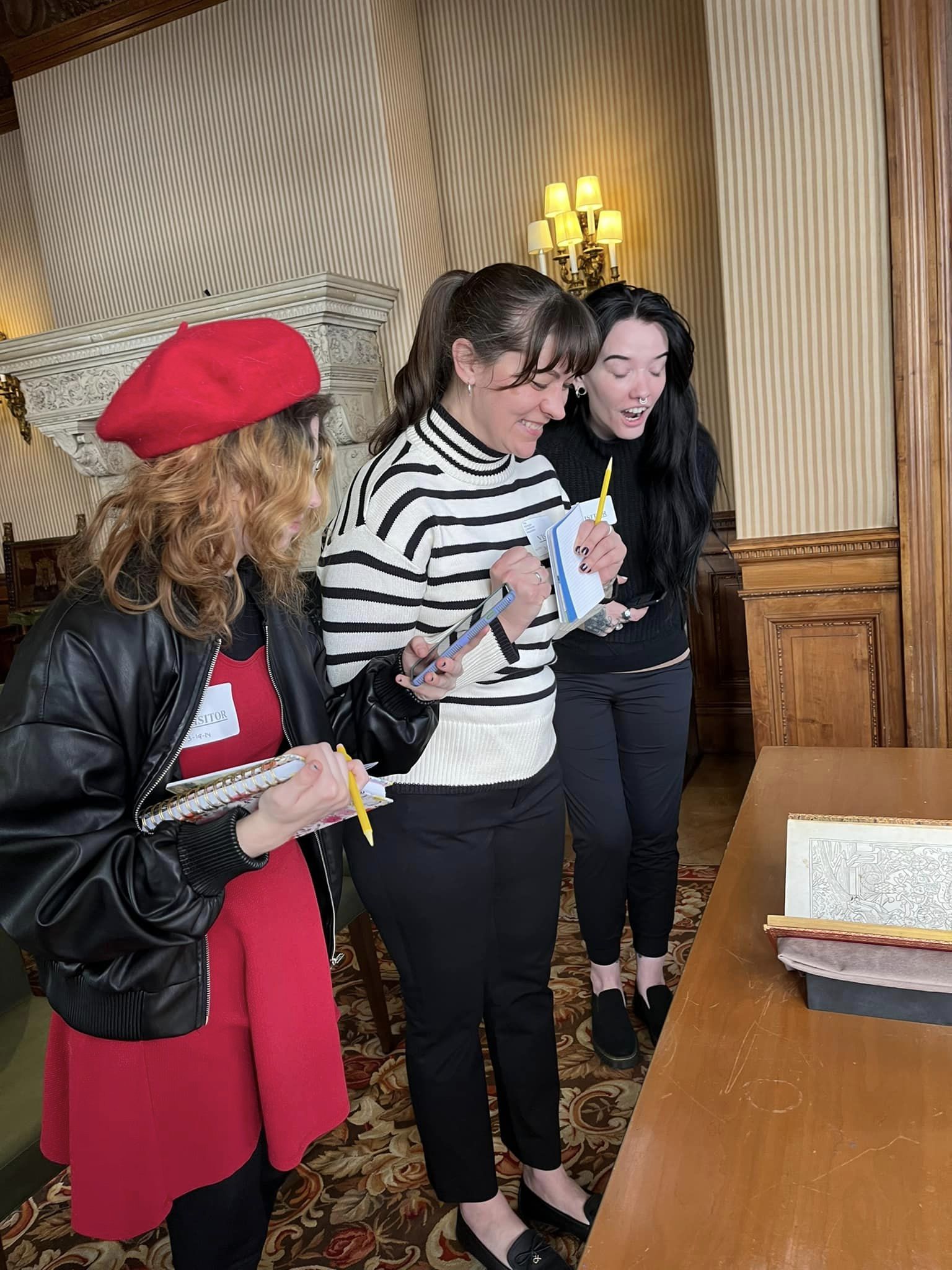 Three students smiling and holding notebooks looking at an old book