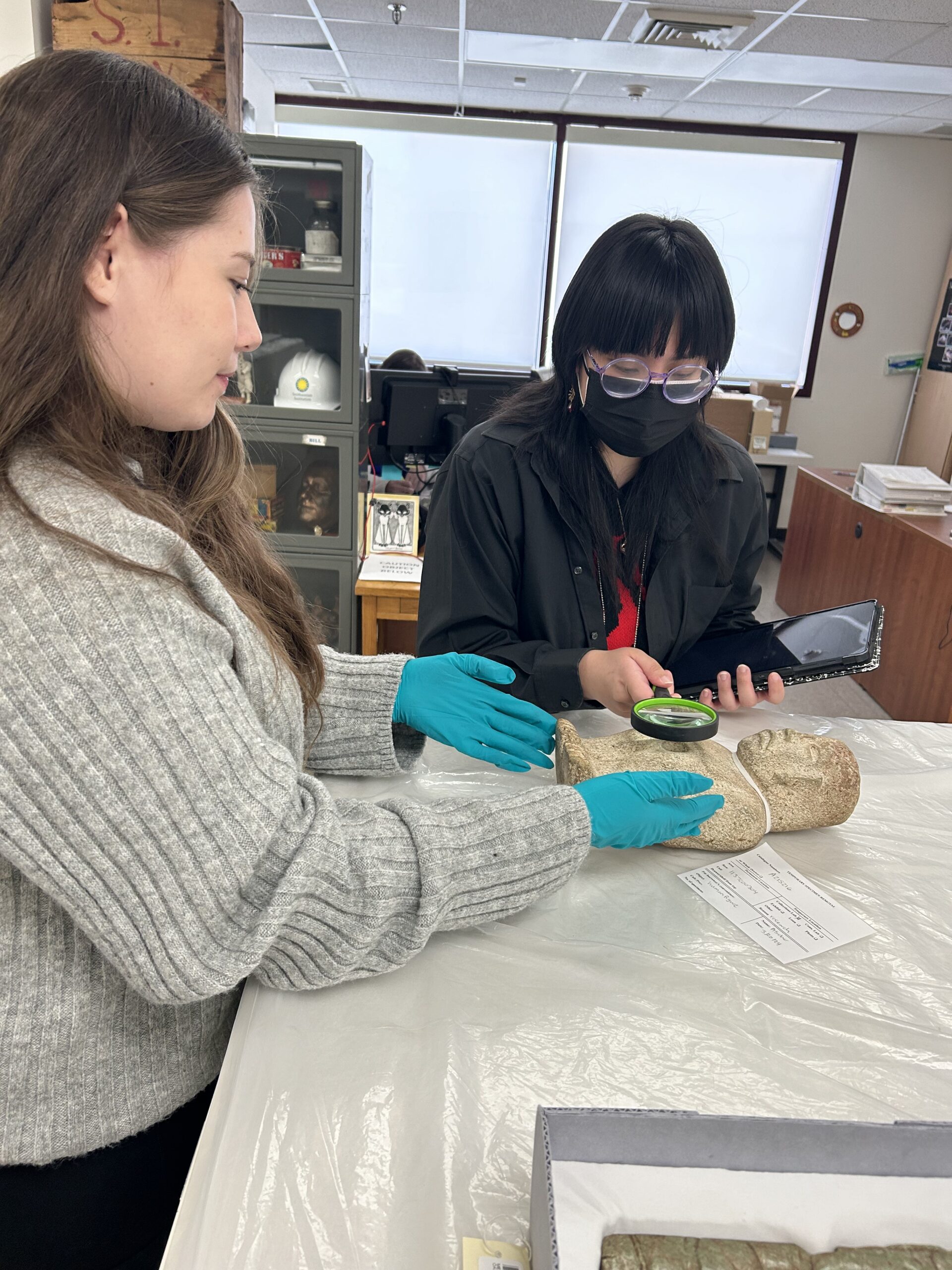 Two MSU Denver students holding magnifying glass looking at a statue