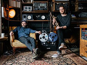 Shadowlands members John Raymond holding a trumpet and Sean Carey sitting in a cozy recording studio