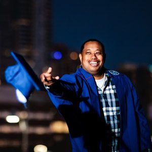 Jameer Fitch wearing his graduation cap and gown at night with the downtown Denver skyline in the background