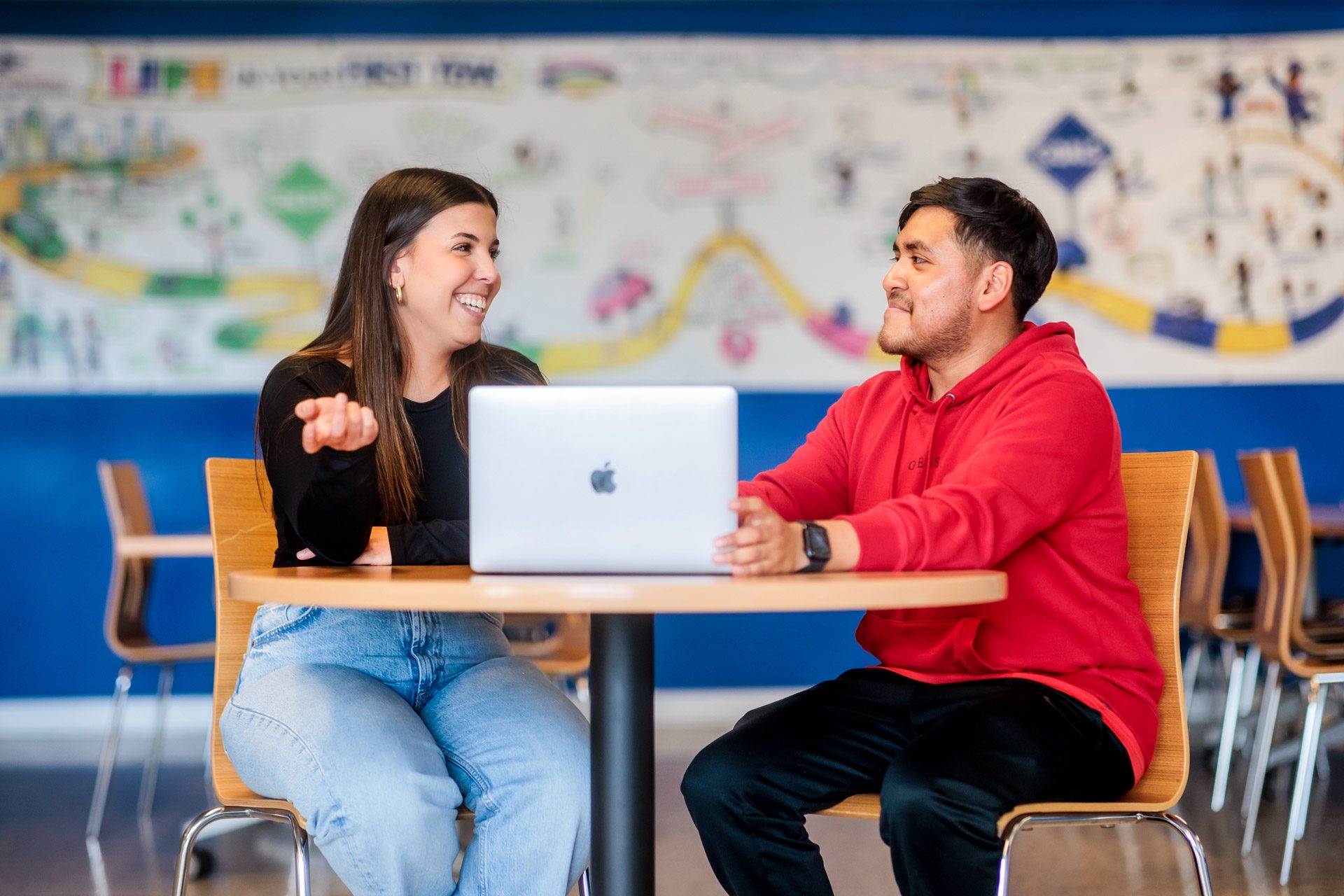 Two students smiling in front of a laptop computer at a table