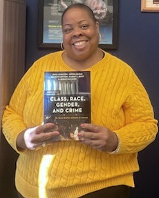 Dr. Cotton posing with new book: Class, Race, Gender, and Crime: The Social Realities of Justice in America.