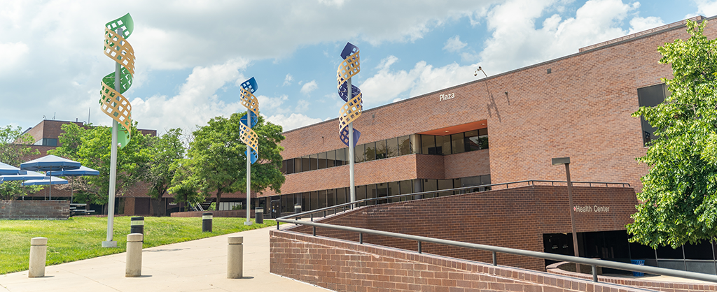 Plaza building with spiral sculptures leading to the entrance on a partly cloudy day.